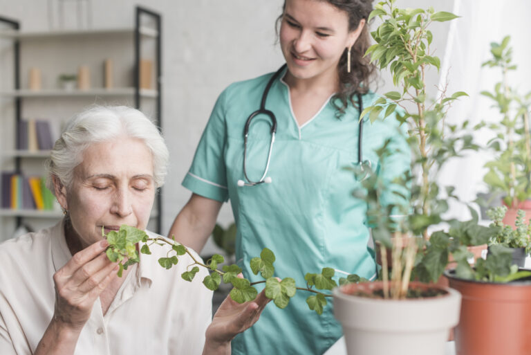 nurse-looking-senior-female-patient-smelling-ivy-plant-pot